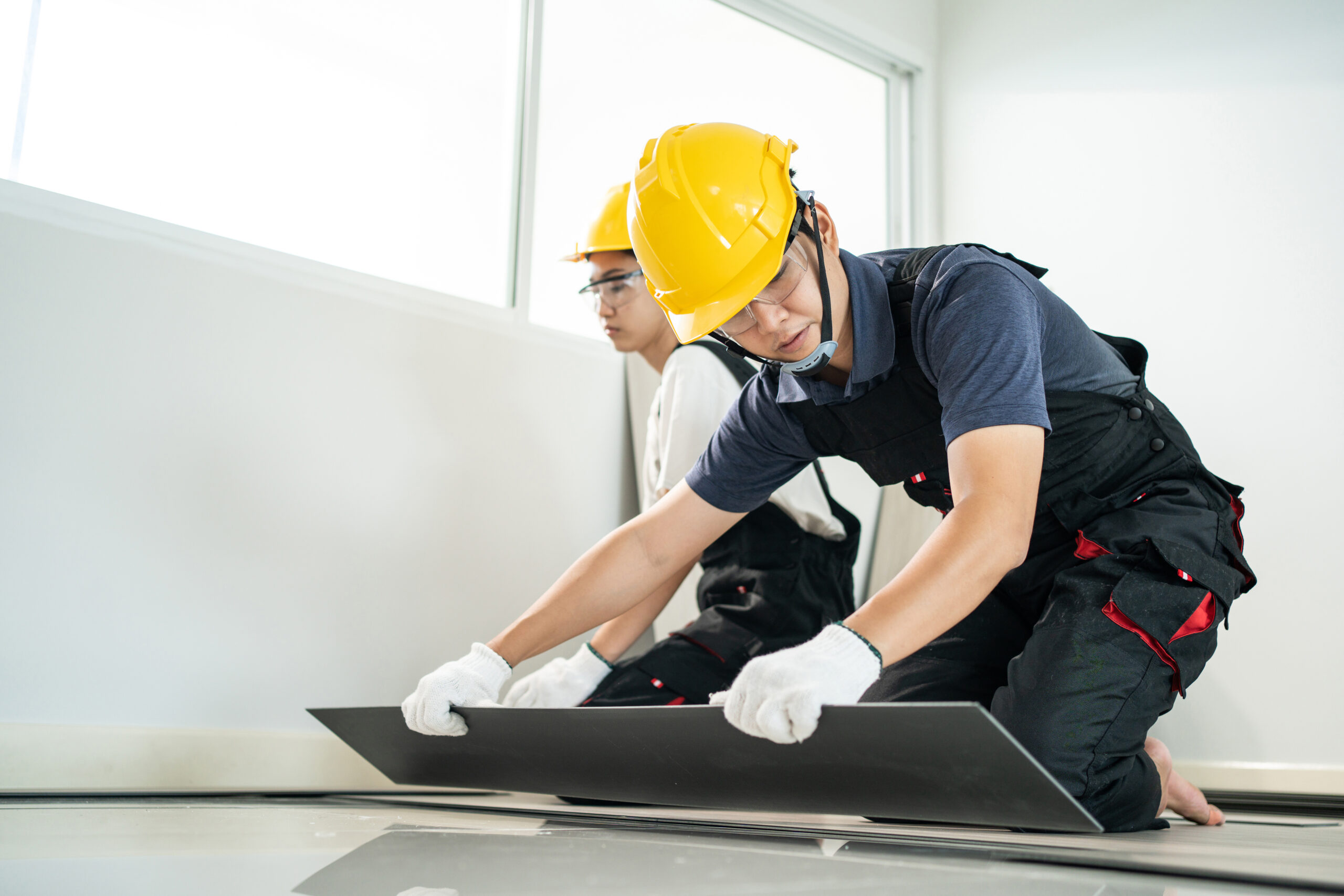 Close-up of Craftsman worker installs laminate board on floor at home. Carpenter worker or Joiner Builder team people wear gloves, work by installs laminate board on corridor floor to renovate house.