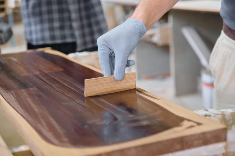 Closeup of workers hand covering wooden plank with finishing protective cover for wood, carpentry furniture woodworking production