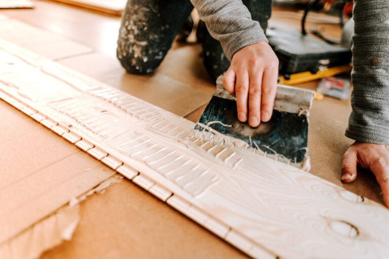 Worker laying and gluing parquet flooring. Worker installing hardwood flooring during house building and construction